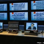 이라크 언론의 자유 수준 - A detailed scene showing a brave Iraqi journalist wearing modest professional attire and glasses, si...